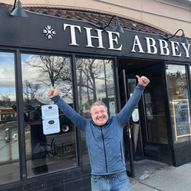 man standing in front of building with two thumbs up smiling